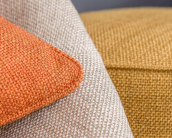 Beige textured chair with orange cushion and mustard decor detail. Maison Mermont.