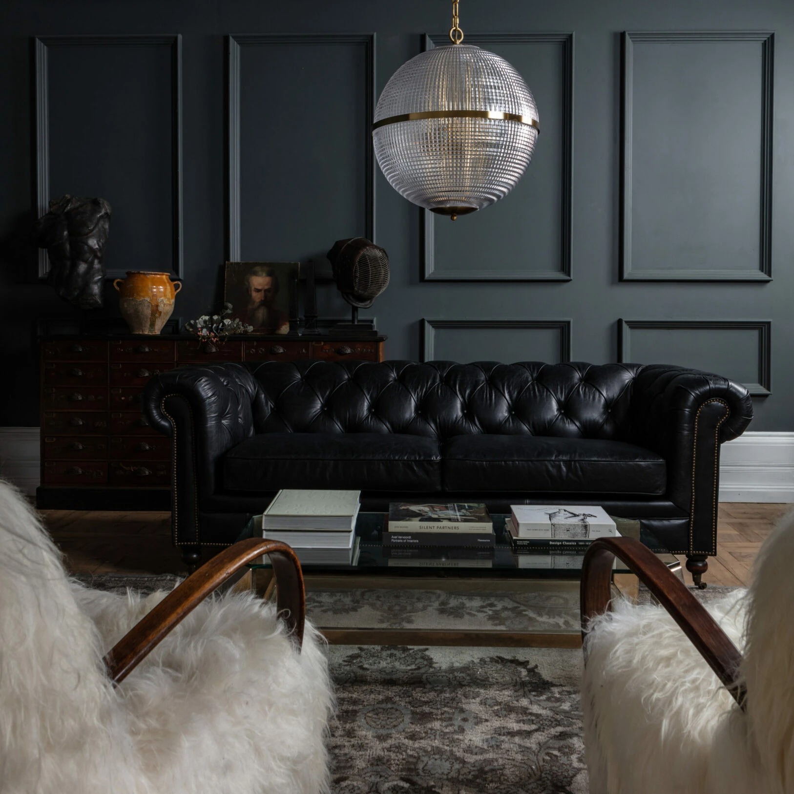 Large Clear Parisian Globe Pendant Elegant black leather chesterfield sofa paired with a modern glass coffee table in a stylishly decorated room. Maison Mermont.