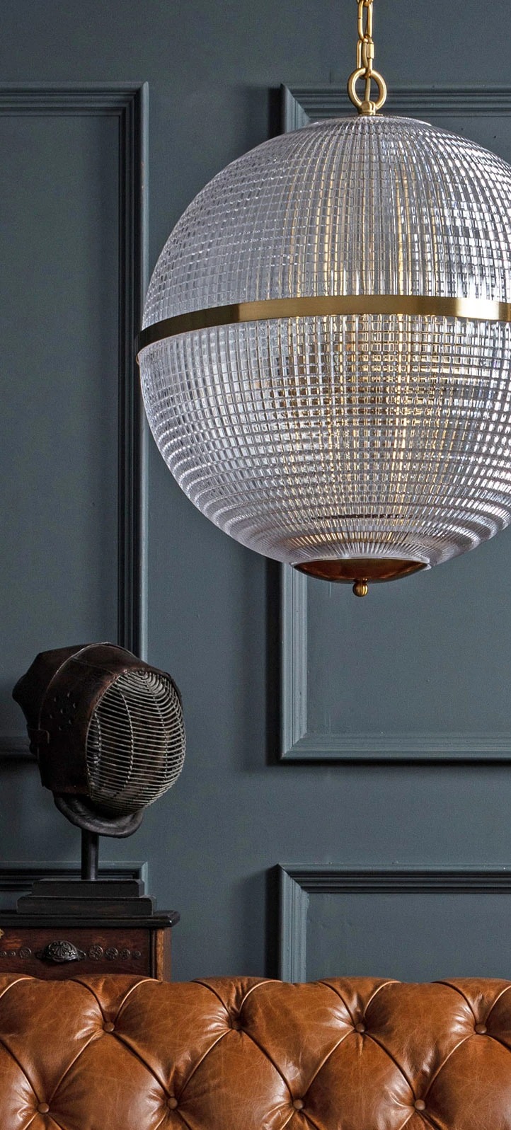Large Clear Parisian Globe Pendant Elegant glass globe pendant light with gold accents, illuminating a stylish interior featuring a brown leather sofa. Maison Mermont.