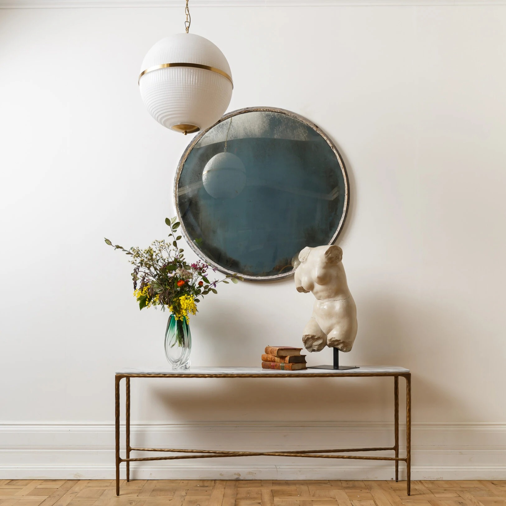 Elegant interior scene featuring a round mirror, floral arrangement, and a sculptural piece on a stylish console table. Maison Mermont.