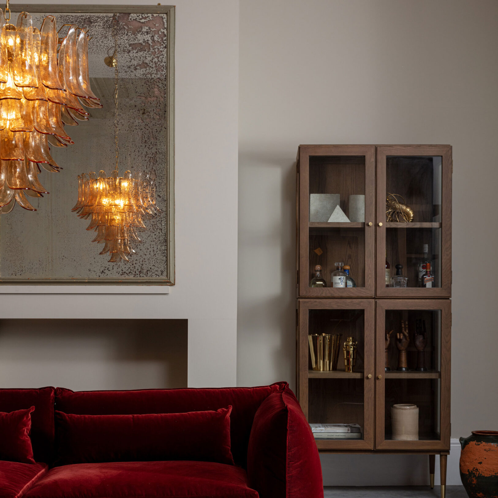 Amber Corolla Large Chandelier Stylish living room featuring a modern glass cabinet and elegant chandeliers, complemented by a plush red couch. Maison Mermont.