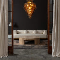 Amber Corolla Large Chandelier Modern living room featuring a plush cream sofa, circular wooden coffee table, and a stunning glass chandelier. Maison Mermont.