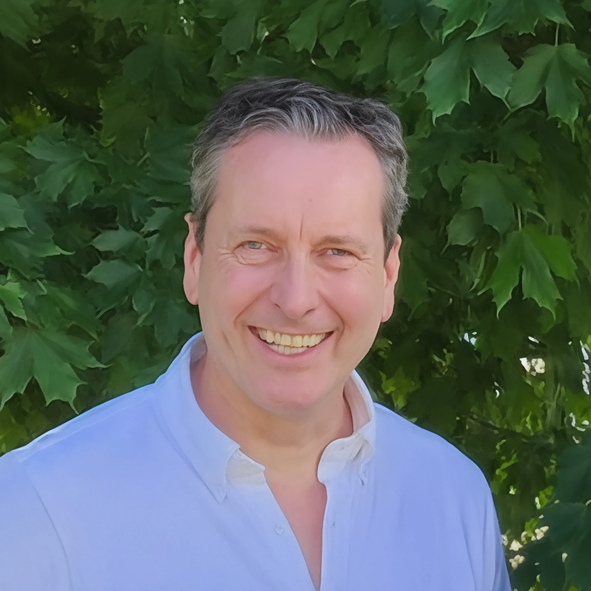 didier for bio 2 Smiling man in a white shirt with green leaves in the background, showcasing a friendly demeanor. Maison Mermont.