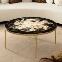 Elegant round coffee table with a geometric inlaid top and gold legs, perfect for modern living spaces. Maison Mermont.