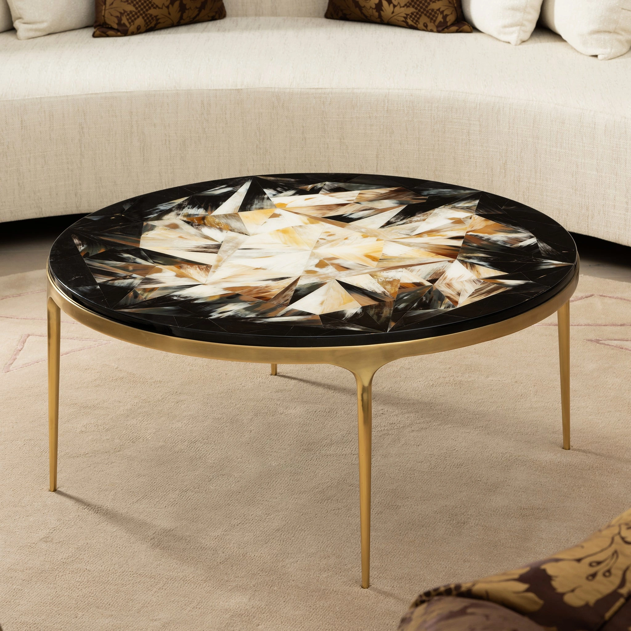 Elegant round coffee table with a geometric inlaid top and gold legs, perfect for modern living spaces. Maison Mermont.