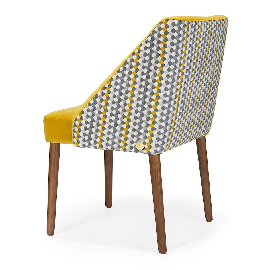 Stylish dining chair with geometric patterned back and yellow upholstery, featuring wooden legs. Maison Mermont.