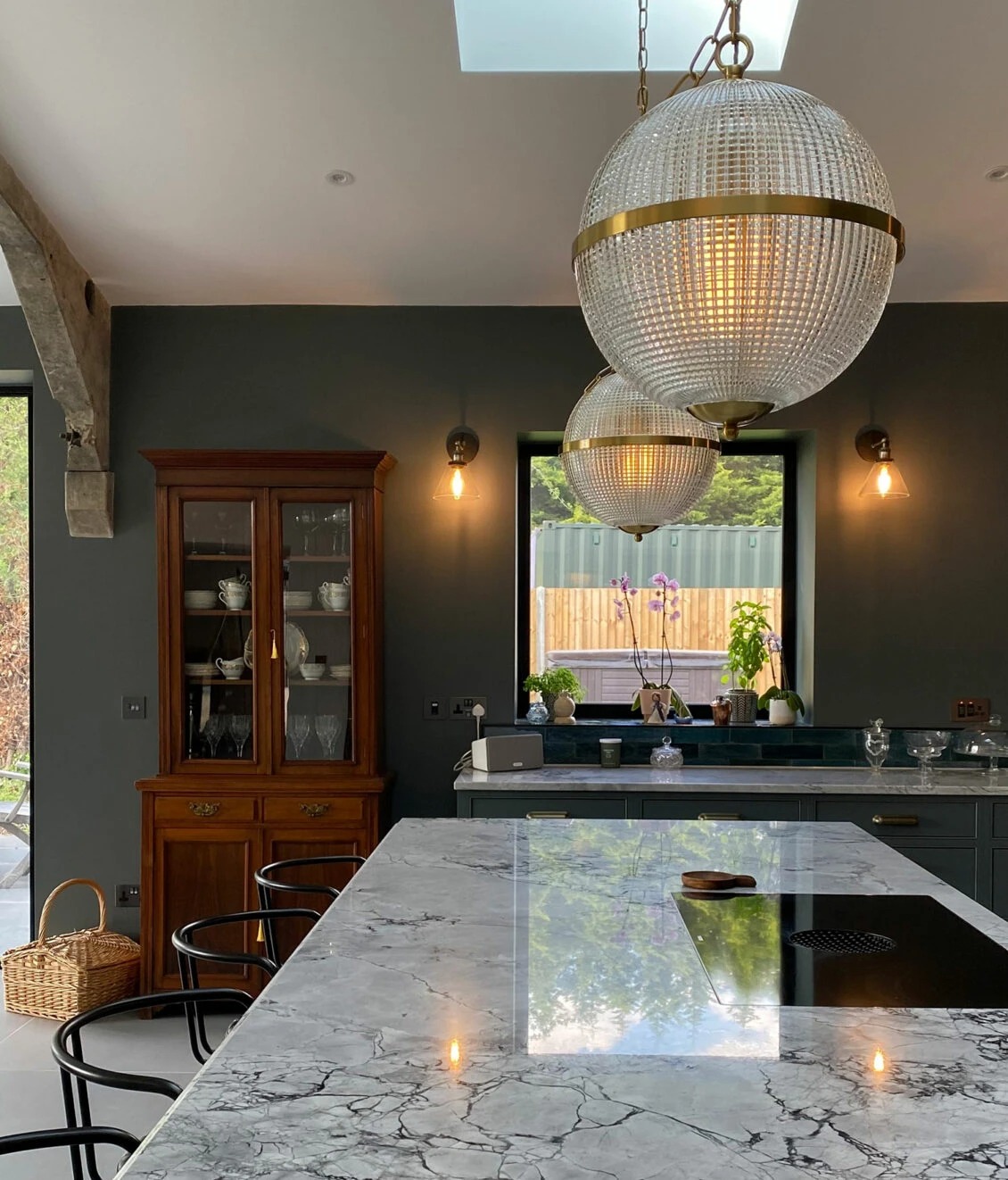 Modern kitchen featuring elegant pendant lights, a marble countertop, and a wooden display cabinet. Maison Mermont.