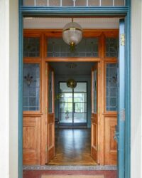 Elegant entrance with wooden doors, stained glass, and stylish lighting leading to a bright interior. Maison Mermont.