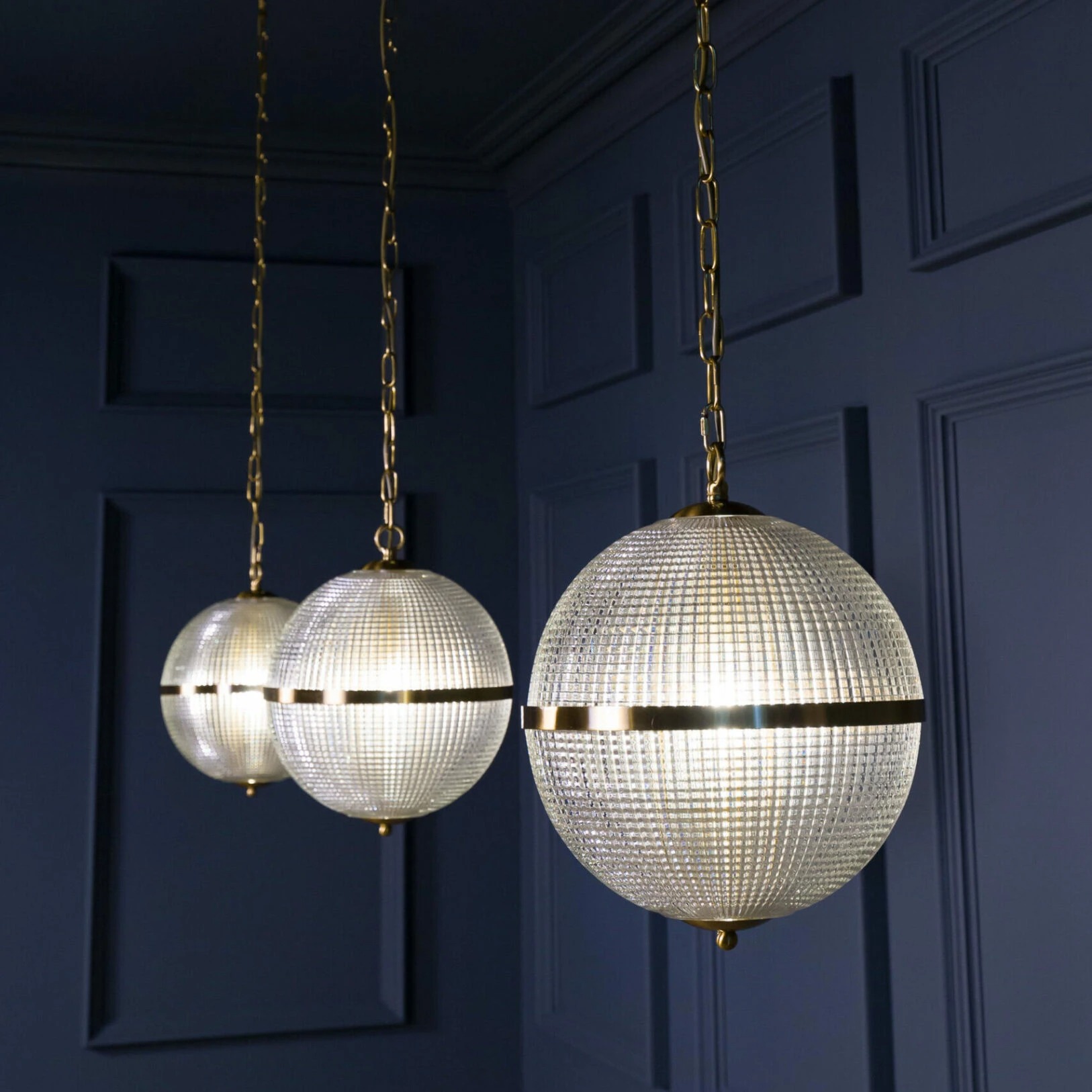 Three elegant globe pendant lights with a textured glass finish and gold accents, perfect for modern decor. Maison Mermont.